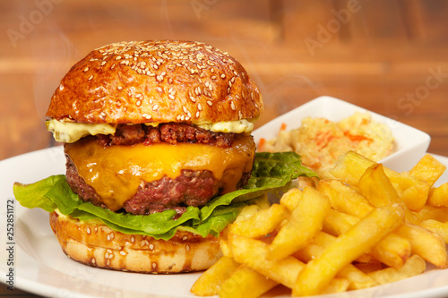 Luxury beef burger in bun with cheese, bacon marmelade, lettuce, french fries and coleslaw salad