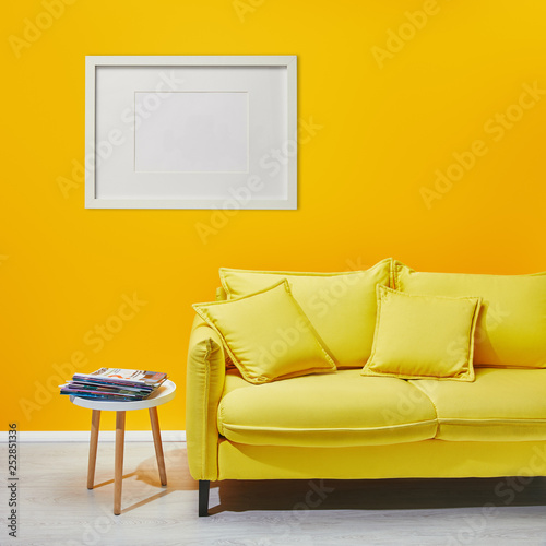coffee table standing near modern yellow sofa near white frame hanging on wall
