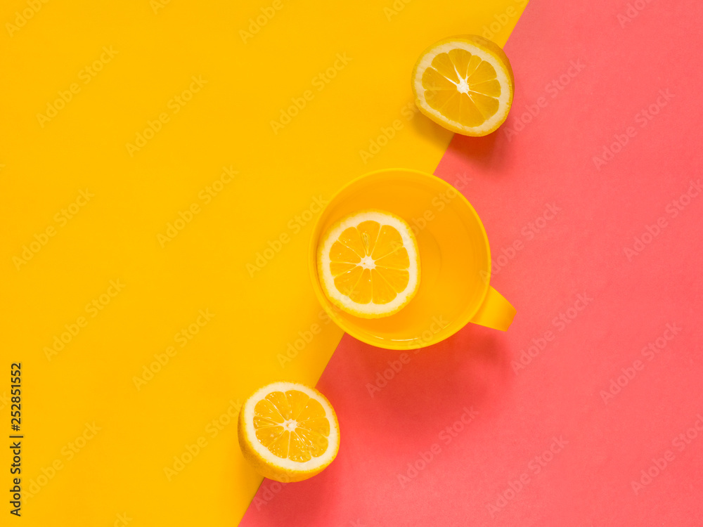 Fototapeta Creative fresh layout. Water with lemon in a yellow mug on a yellow and pink geometric background. Healthy drink, live water, lemonade. Biohacking minimalist concept. Flat lay