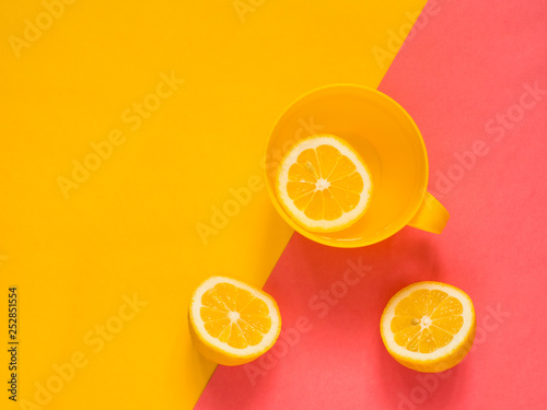 Creative fresh layout. Water with lemon in a yellow mug on a yellow and pink geometric background. Healthy drink, live water, lemonade. Biohacking minimalist concept. Flat lay