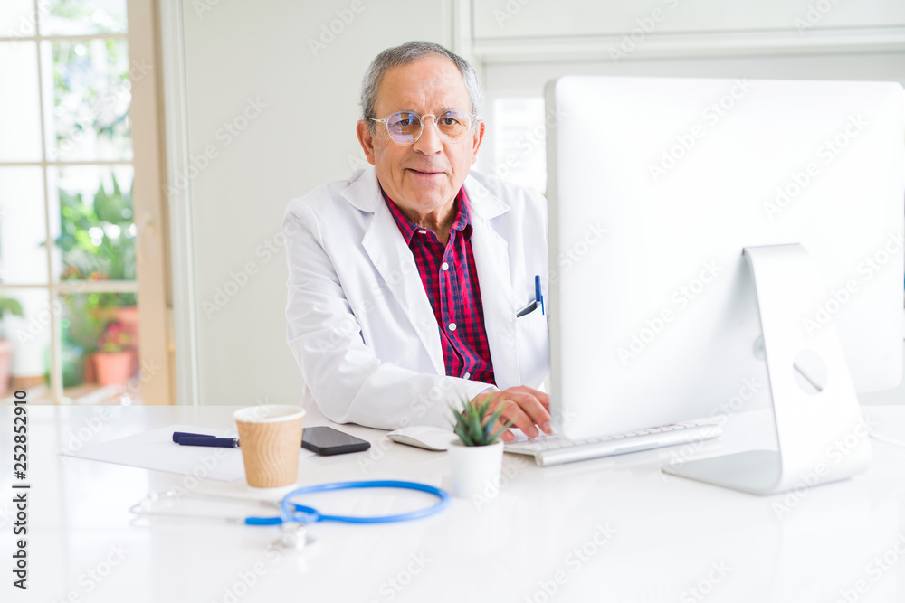 Senior doctor man at the clinic working with computer and smiling