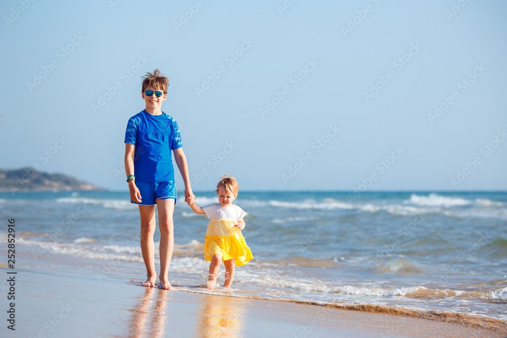 Kids playing on tropical beach. Big brother together with his little sister at sea shore at sunset. Family summer vacation. Children play with water. Ocean and island fun Kids playing on tropical beach. Big brother together with his little sister at sea shore at sunset. Family summer vacation. Children play with water. Ocean and island fun