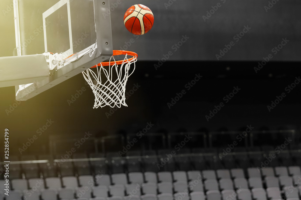 Basketball ball flies into the basketball hoop on the background of the stands of the sports complex. Toned