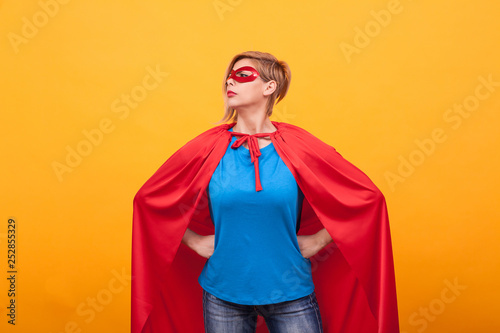 Young woman in superheros costume standing proudly over yellow background