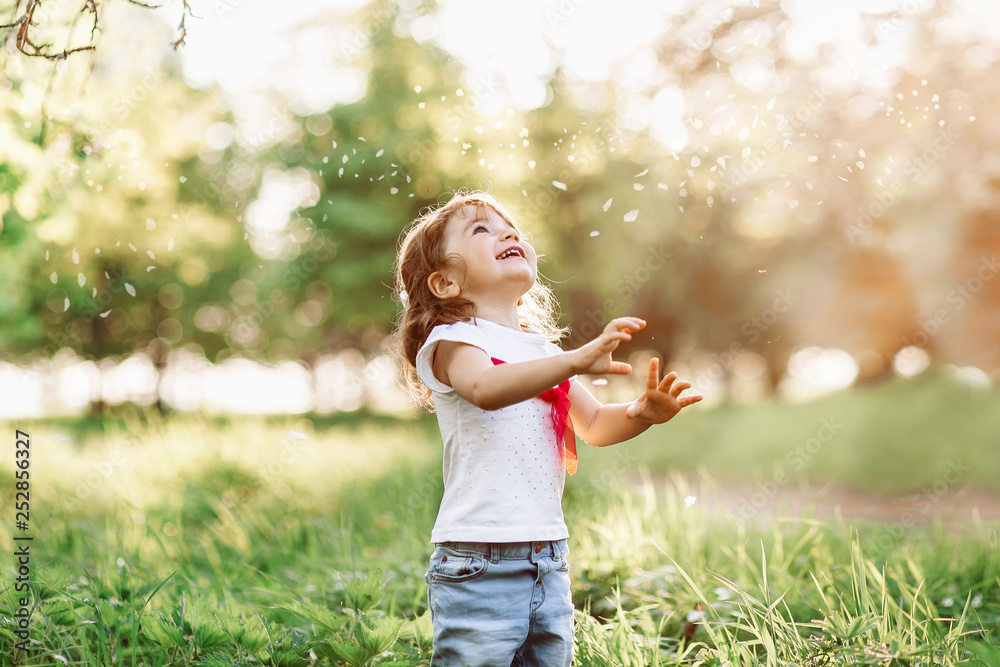 A portrait of a cute little girl smiling in the garden on a nice summer day and looking at a falling petals flower A portrait of a cute little girl smiling in the garden on a nice summer day and looking at a falling petals flower