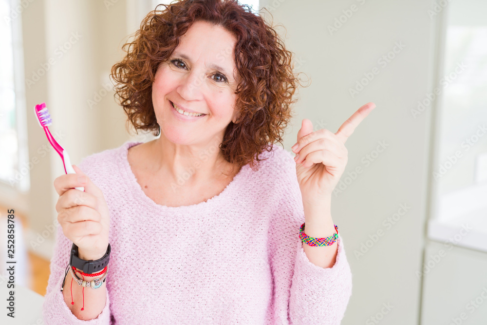 Senior woman holding pink toothbrush at dental clinic very happy pointing with hand and finger to the side Senior woman holding pink toothbrush at dental clinic very happy pointing with hand and finger to the side