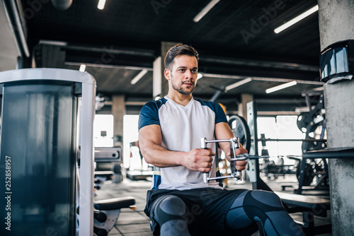 Portrait of athletic man exercising in the gym, improving his arm muscles and body.