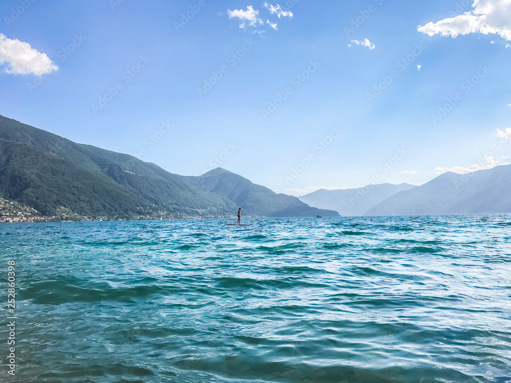 unknown person standing on paddle board in the middle of the sea against the backdrop of mountains