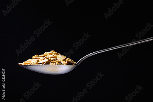 Metal silver spoon with the oatmeal in it. Large side view. Black dark background. Plenty of room for text.
