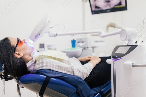 Portrait of a female patient at dentist in the clinic. Teeth whitening procedure with ultraviolet light UV lamp.
