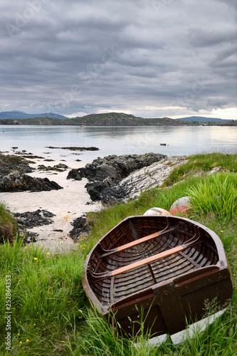 Fotografia Sand beach and rocky shore of Isle of Iona with beached boat and view of Fionnph