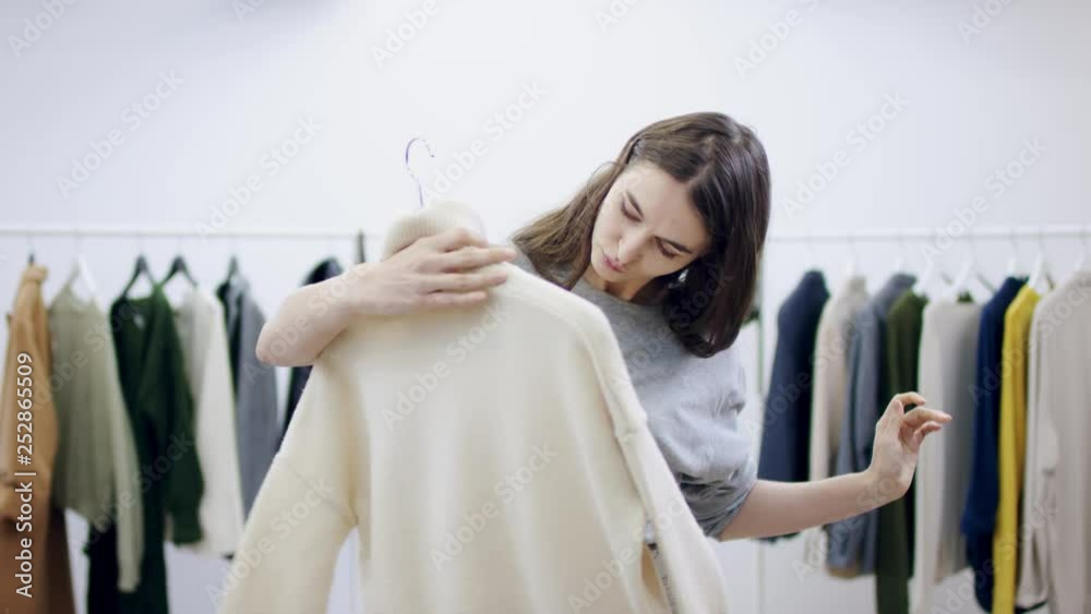 Mean young woman examines a sweater in a clothing room Mean young woman examines a sweater in a clothing room
