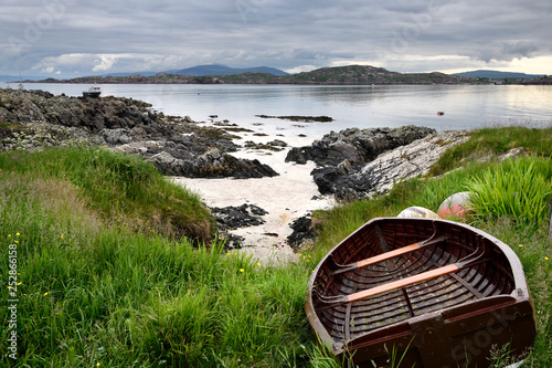 Fotografie Rocky shore of Isle of Iona with beached boat with Fionnphort Isle of Mull and m