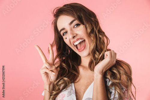 Image of amusing woman 20s wearing dress smiling and showing peace sign
