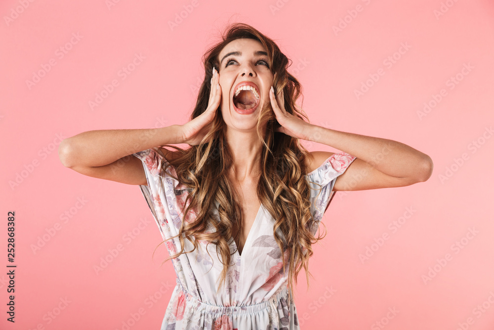 Portrait of positive woman 20s with long hair wearing dress standing and screaming isolated over pink background Portrait of positive woman 20s with long hair wearing dress standing and screaming isolated over pink background