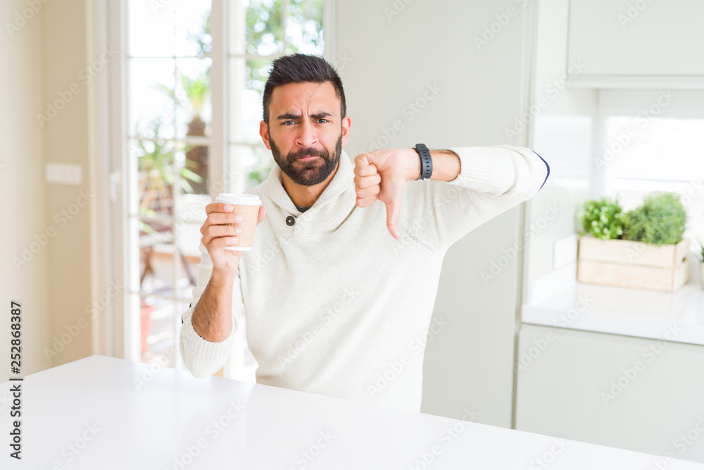 Handsome hispanic man drinking a coffee in a paper cup with angry face, negative sign showing dislike with thumbs down, rejection concept