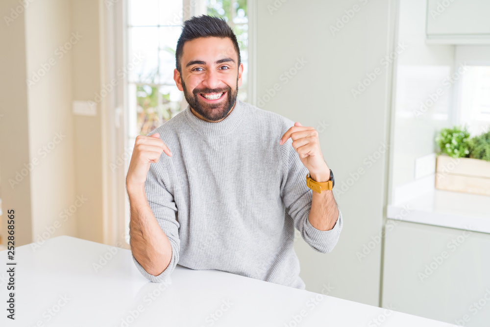 Handsome hispanic man wearing casual sweater at home looking confident with smile on face, pointing oneself with fingers proud and happy.