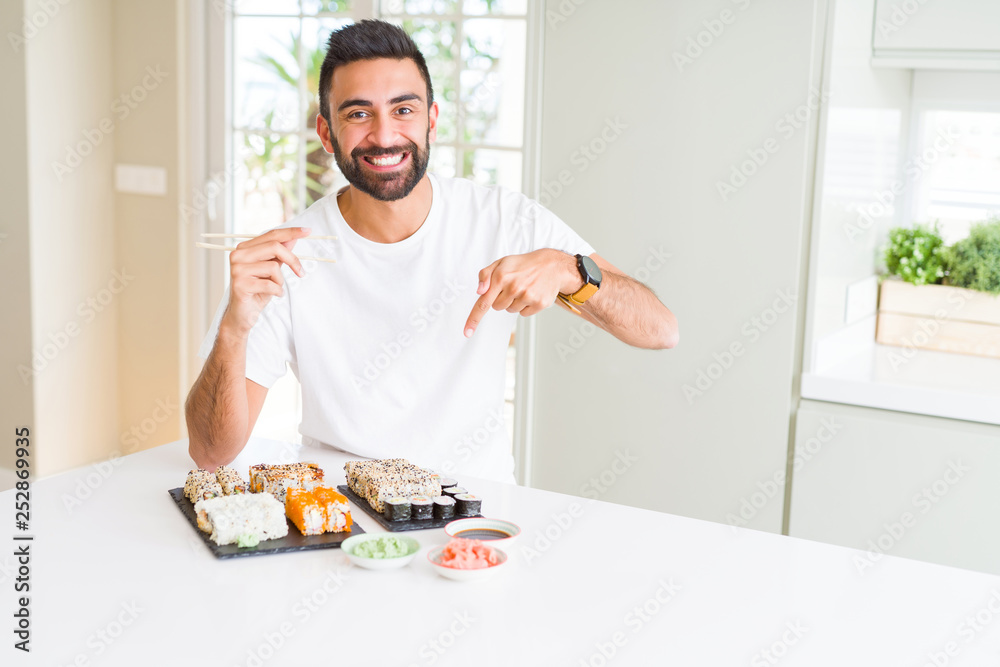 Handsome hispanic man eating asian sushi using chopsticks very happy pointing with hand and finger Handsome hispanic man eating asian sushi using chopsticks very happy pointing with hand and finger
