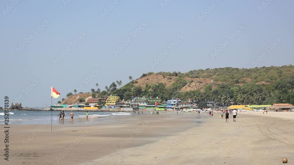 sandy beach against the sea and colored houses on a hill, people walking along the beach and swimming in the ocean sandy beach against the sea and colored houses on a hill, people walking along the beach and swimming in the ocean