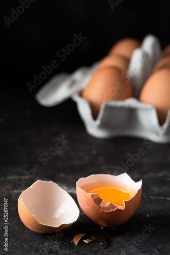 offenes Ei mit Eigelb in Schale auf dunklem Hintergrund mit Eiern und Karton hochformat