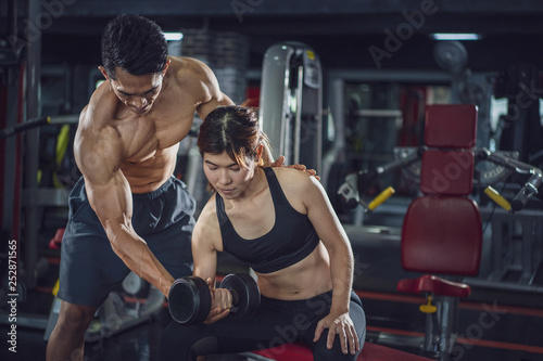 Young woman exercise in a gym with the help of her personal trainer, Fitness instructor exercising with his client at the gym, Personal trainer helping woman working with heavy dumbbells