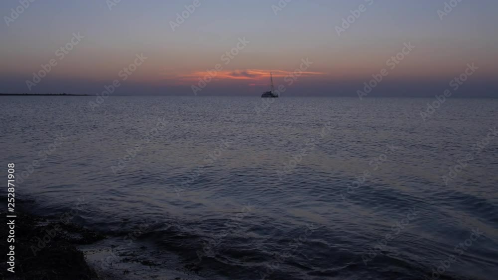 sunset over the calm surface of the sea, a lonely yacht and the movement of the setting sun through the clouds over the sea horizon sunset over the calm surface of the sea, a lonely yacht and the movement of the setting sun through the clouds over the sea horizon
