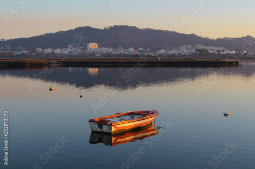 Small boat in the river, with mountain and biuldings on background. Reflection on the water