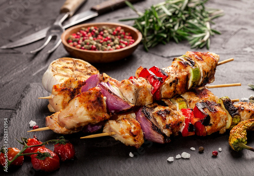 Grilled chicken skewers with spices and vegetables on black background