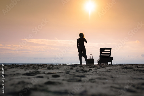 Woman standing near sun lounger and taking off her clother. Beach at sunset. Summer concept.