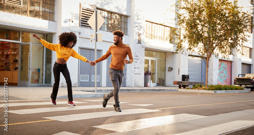 Photos Fashionable young black couple running across a city street holding hands, full