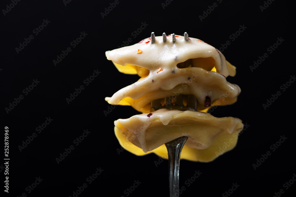 Naklejka premium Ravioli in Cheese Sauce Speared on Fork with Black Background