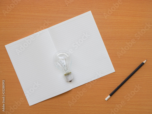 top view of notebook, light bulb and pencil on wooden table with copy space