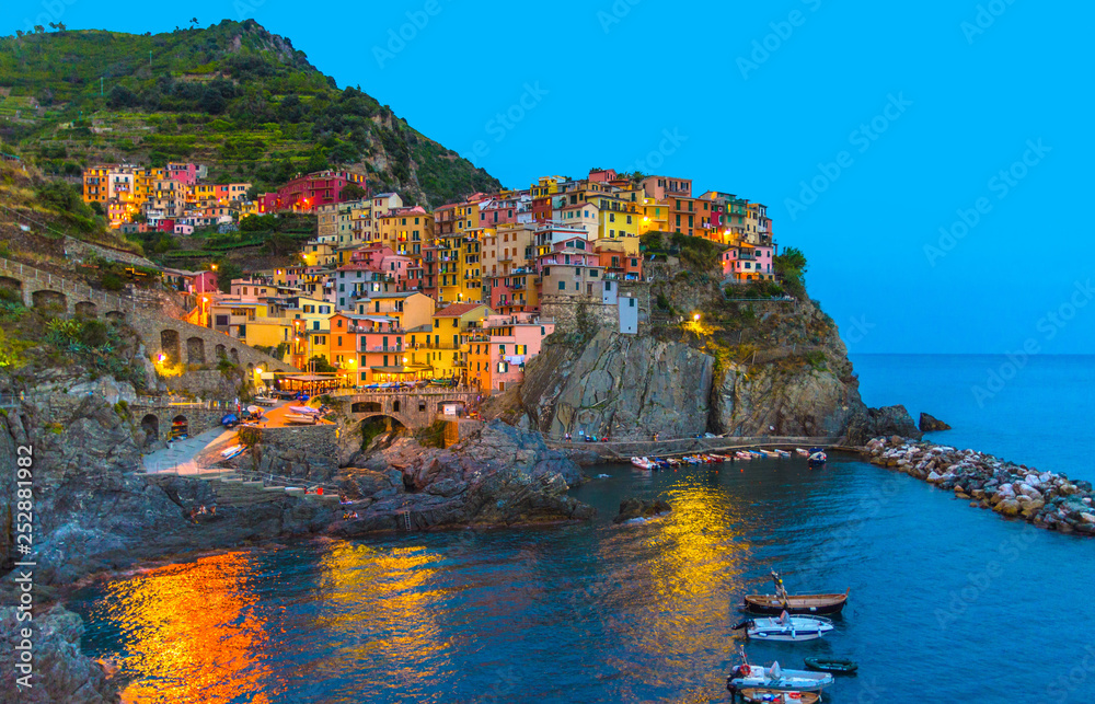 Manarola traditional typical Italian village in National park Cinque Terre with colorful multicolored buildings houses on rock cliff and marine harbor, night evening view, La Spezia, Liguria, Italy