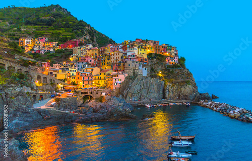 Manarola traditional typical Italian village in National park Cinque Terre with colorful multicolored buildings houses on rock cliff and marine harbor, night evening view, La Spezia, Liguria, Italy