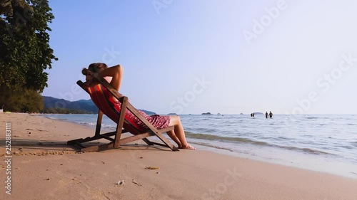 Young woman resting on the beach sitting in deck chair bare foot in the waves, warm summer vacation holidays sea landscape, relaxing outdoor lifestyle