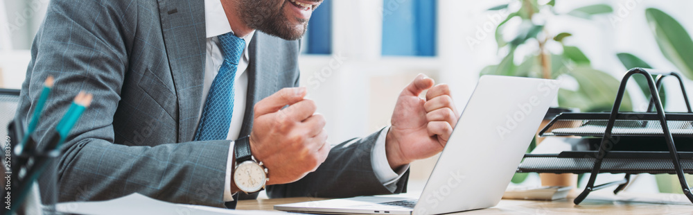 cropped view of businessman sitting at table with laptop and showing yes gesture in office