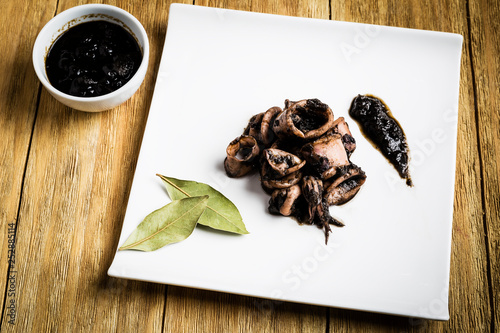 squid cooked on a white plate next to a bowl with ink and some bay leaves photo