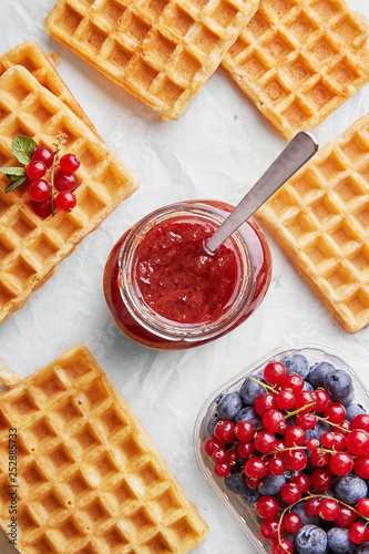 Belgian waffle with jar full of jam and decorated with fruits on a marble background viewed from above. Top view
