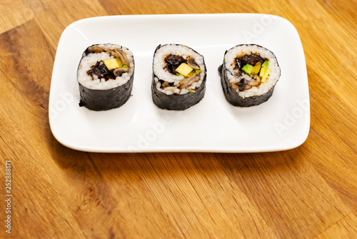 Homemade vegan Sushi rolls filled with avocado on a small plate on a wooden table with soy sauce, wasabi and ginger