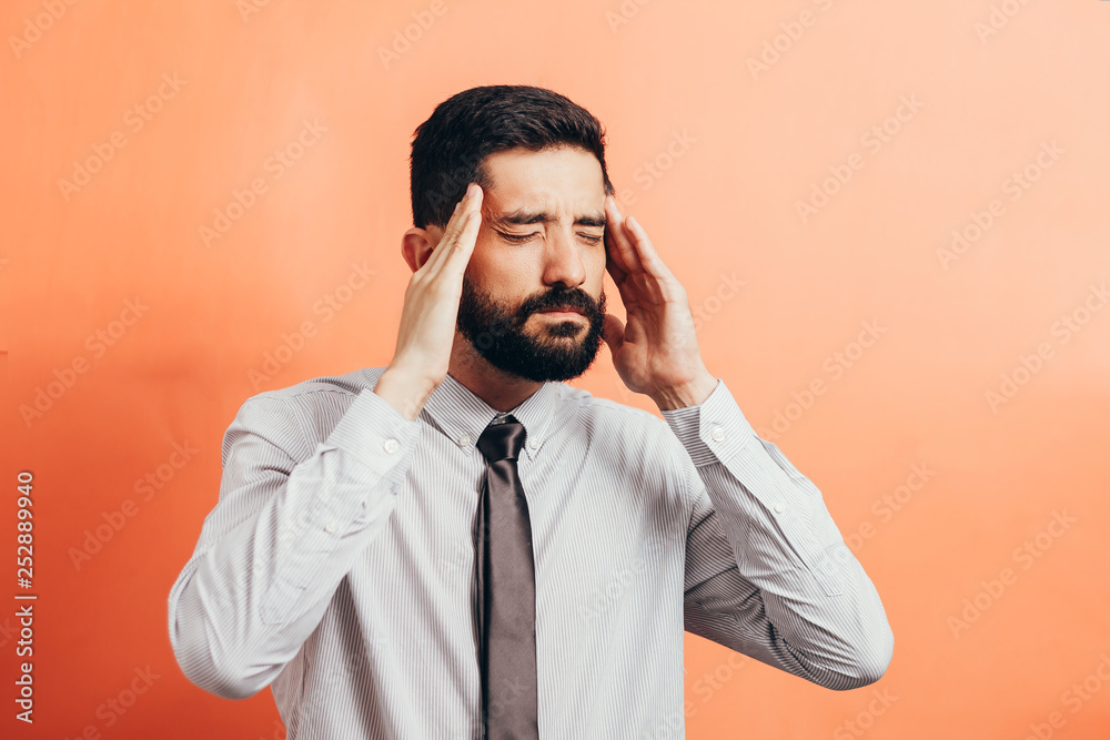Portrait of an annoyed businessman suffering from a headache isolated on color background Portrait of an annoyed businessman suffering from a headache isolated on color background