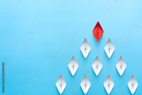 Fototapeta Naklejka Na Ścianę i Meble -  Leadership concept. Red leader paper ship leading among white on blue background. copy space