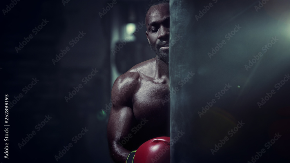 Hands of boxer over dark gym background. Strength, attack and motion concept. Fit african american model in movement. Naked muscular athlete in red gloves. Sporty man during boxing Hands of boxer over dark gym background. Strength, attack and motion concept. Fit african american model in movement. Naked muscular athlete in red gloves. Sporty man during boxing