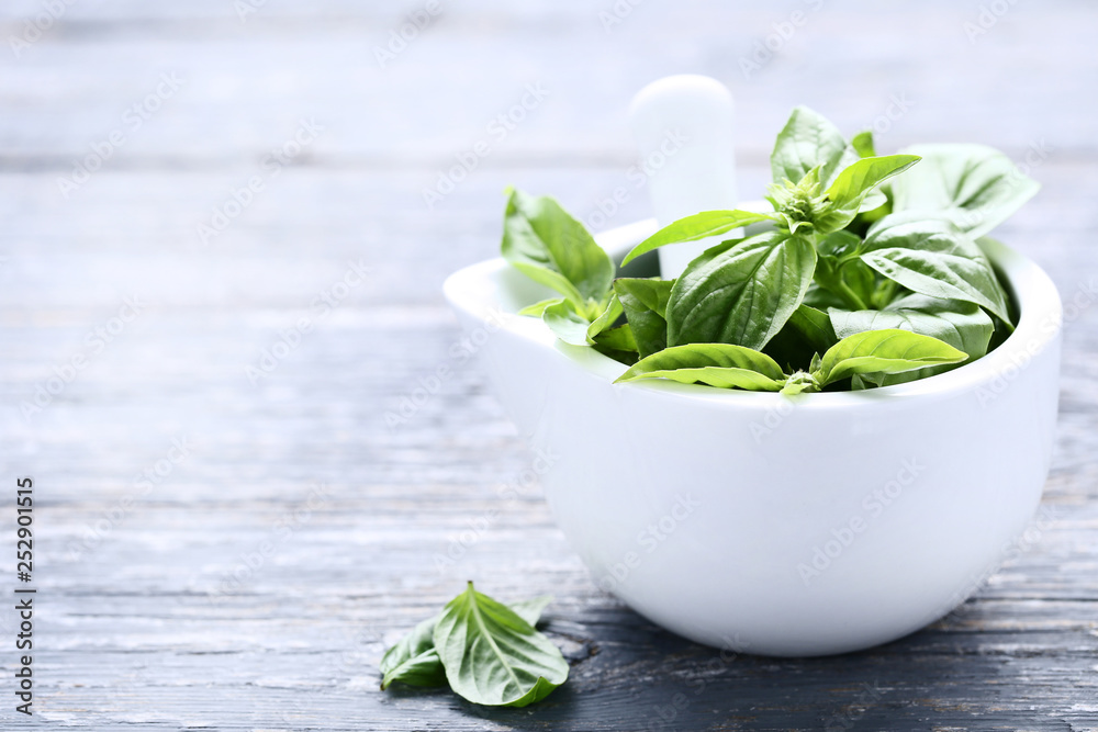 Green basil leafs in mortar on grey wooden table Green basil leafs in mortar on grey wooden table
