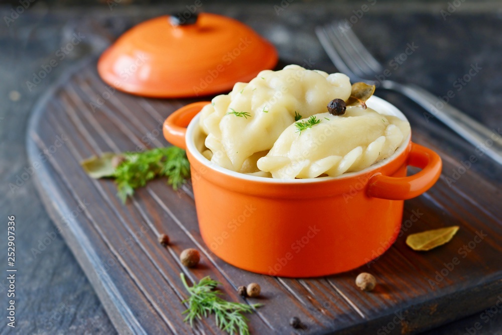 Dumplings with potatoes with herbs, spices and butter in a ceramic portion pot on a dark background. Varenyky, vareniki, pierogi, pyrohy - dumplings with filling. Dumplings with potatoes with herbs, spices and butter in a ceramic portion pot on a dark background. Varenyky, vareniki, pierogi, pyrohy - dumplings with filling.