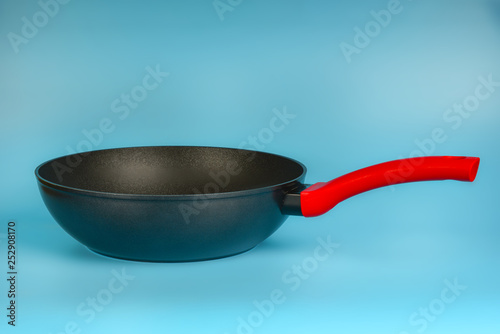 Black iron deep pan with a red handle on a blue background