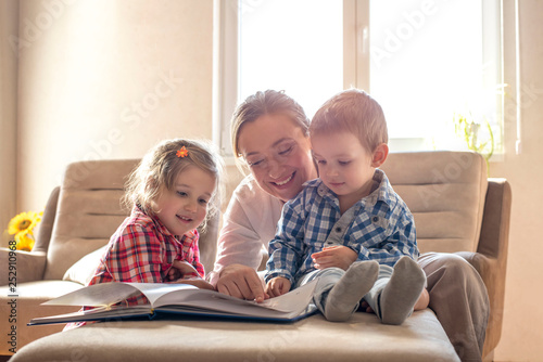 Mother and children reading book and having fun while spending time together at home