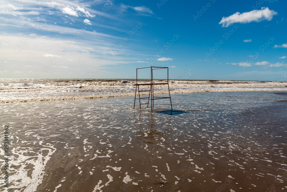 Empty beach in Argentina with high tide with a red lifeguard stand made of tubes with some clouds