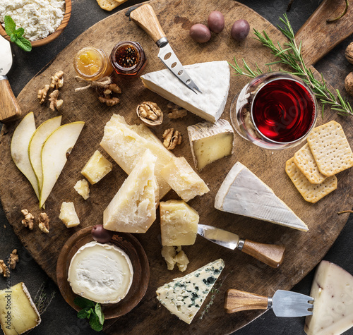 Cheese platter with different cheeses, fruits, nuts and wine on stone background. Top view. Tasty cheese starter.