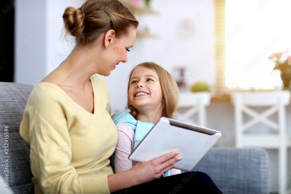 Little girl and her mom using tablet while sitting on sofa at home Little girl and her mom using tablet while sitting on sofa at home