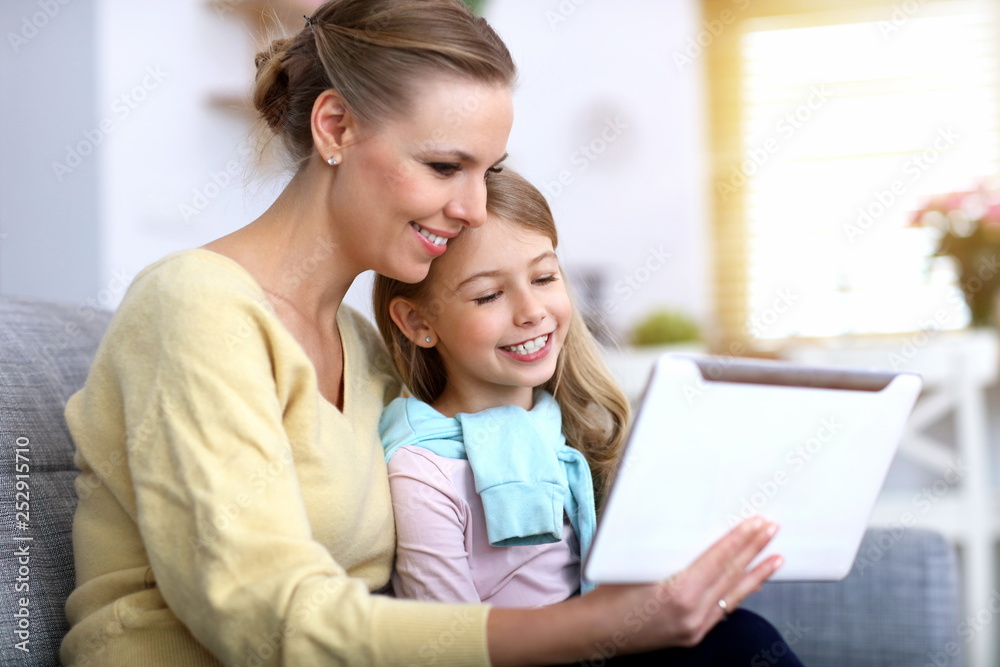 Little girl and her mom using tablet while sitting on sofa at home Little girl and her mom using tablet while sitting on sofa at home